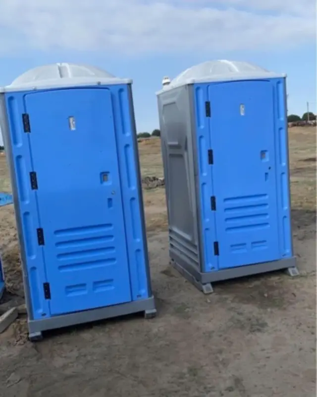 Two blue standard porta potties set on a dirt jobsite pad